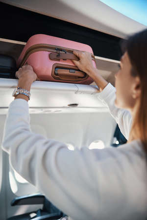 Female is putting suitcase into luggage rackの写真素材