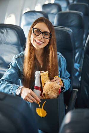 Traveller on airplane smiling at camera while opening shopping bag