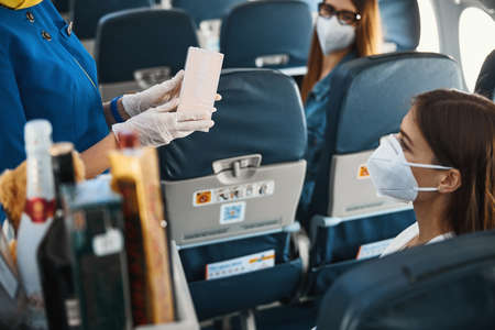 Female airline steward presenting box of cookies to womanの写真素材