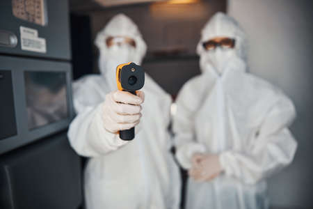 Two people in white coveralls pointing with temperature gun