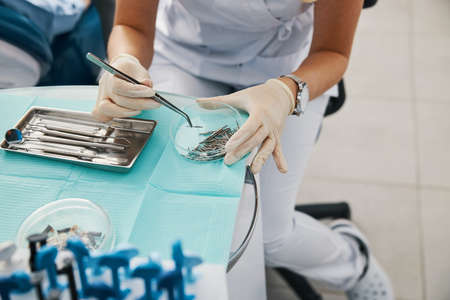 Dentist picking up dental bur with cotton forceps from tray