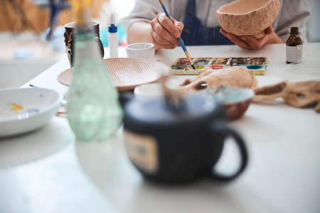 Adult reaching for paint with brush during pottery paintingの写真素材