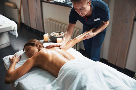 Beautiful caucasian woman under the towel relaxing while getting manual massage in spa salonの写真素材