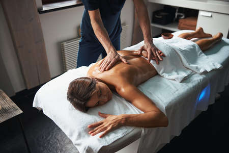 Beautiful young woman under the towel relaxing at the back massage at spa salonの写真素材