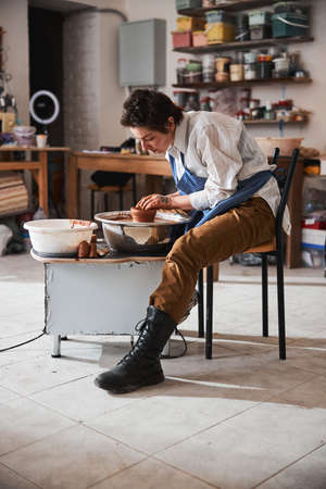 Concentrated brunette woman creating new pot in workshop