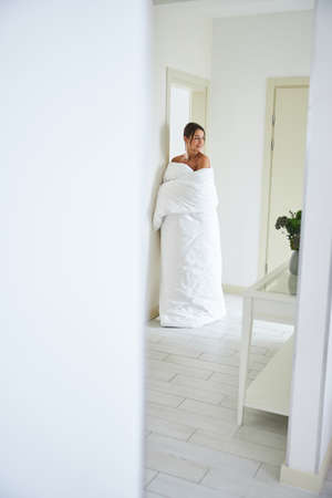 Pretty young elegant female in quilt posing at the photo camera in modern cozy room interiorの写真素材