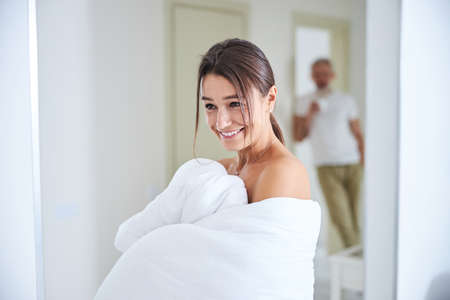 Brunette caucasian female covered in quilt in room indoorsの写真素材
