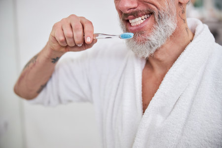 Handsome adult male in plush bathrobe brushing hos teeth in bathroomの写真素材