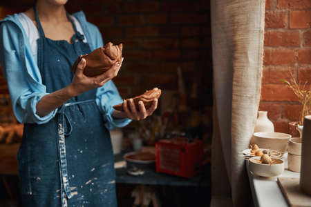 Beautiful elegant woman artisan with pieces of earthenware product in arms in cozy home workshopの写真素材