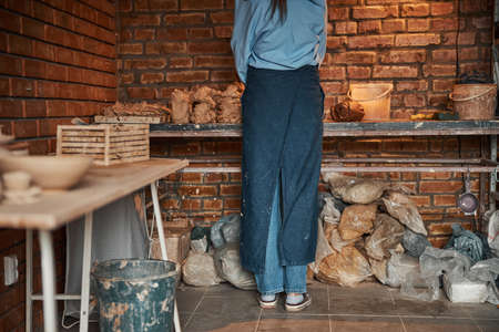 Beautiful elegant young ceramicist squeezing piece of earthenware product in pottery cozy workshopの写真素材