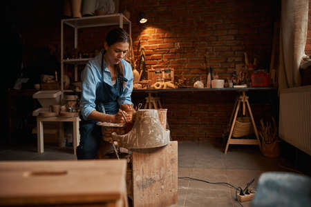 Happy attractive focused ceramicist working with earthenware tableware on pottery wheel in workshopの写真素材