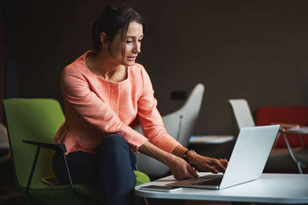 Beautiful brunette female in formal clothes surfing internet while sitting in co-working space
