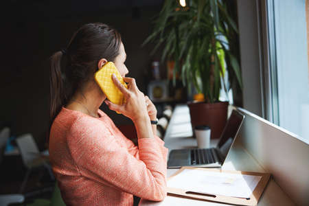 Beautiful elegant female entrepreneur looking away while talking on mobile phone in room indoorsの写真素材