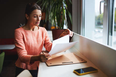 Seriously Caucasian female entrepreneur reading agreements and sighing it in modern luxury office