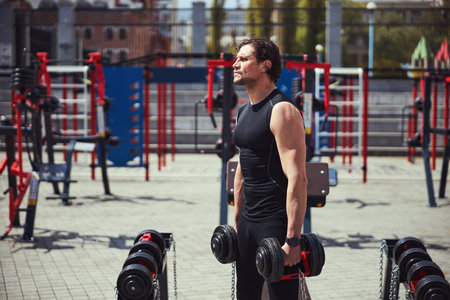 Strong male lifting heavy dumbbells on sports groundの写真素材