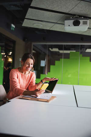 Beautiful elegant young Caucasian female entrepreneur reading message on cell phone in the bright officeの写真素材