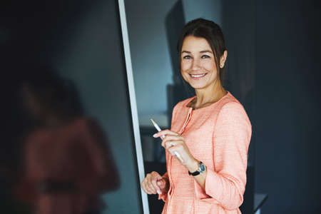 Young cheerful Caucasian business lady posing at the photo camera in the modern luxury officeの写真素材