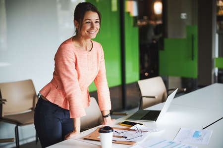 Brunette attractive female office worker with laptop and documents on the table in the co-worker...