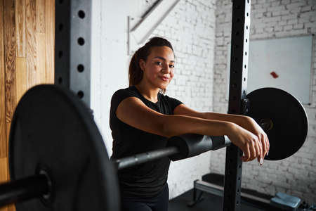 Smiling young woman exercising with barbell indoors