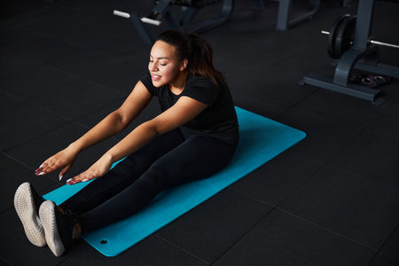 Happy young woman doing stretching in gymの写真素材