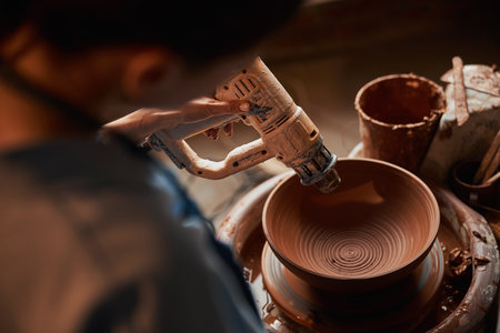 Unrecognized female artisan sitting on the pottery wheel while making clay bowl in art studioの写真素材