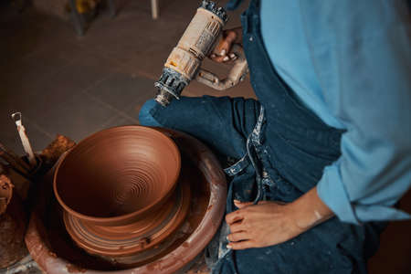 Elegant pretty craft woman holding blowtorch in hand while making clay bowl in pottery workshop