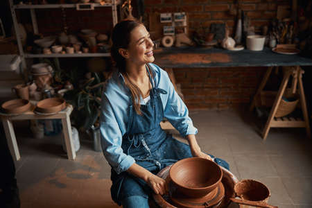 Beautiful elegant Caucasian female artisan working on pottery wheel in workshopの写真素材