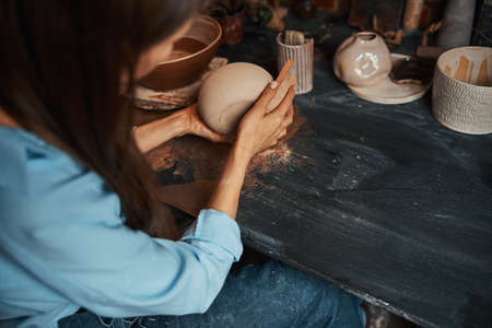 Beautiful elegant ceramicist sitting at the work desk modeling ceramic and clay bowl in art studioの写真素材