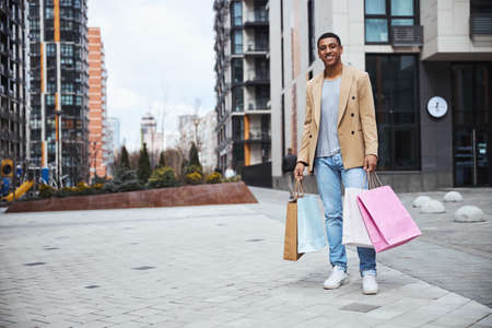 Delighted dark-skinned freelancer standing with his purchasesの写真素材