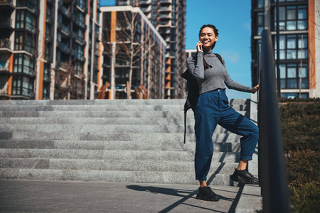 Joyful woman leaning on the metal handrail during the phone conversationの写真素材