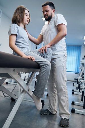 Osteopath doctor checks knee joint of girl sitting on massage bed closeup. Pediatric physiotherapistの写真素材