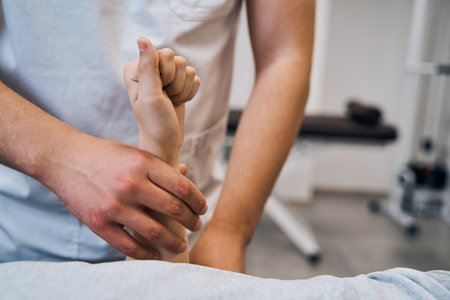Pediatric physiotherapist in uniform checks girls arm on massage bed closeup. Professional therapistの写真素材