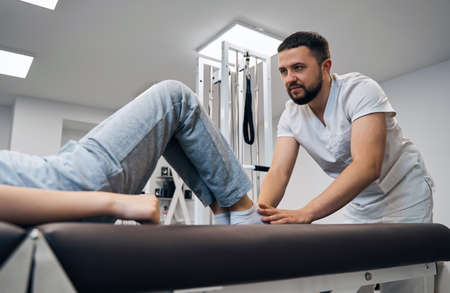 Physiotherapist treatments kids knee on massage therapy bed. Chiropractor tests patient sport injuryの写真素材