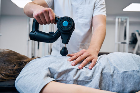 Massage therapist with massagers percussion gun treats girls back and spine on therapy sessionの写真素材