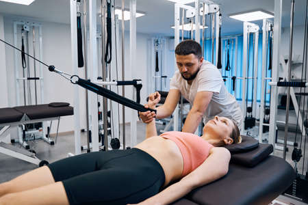 Young woman on massage bed with expander simulator. Physical therapist treat injury to shoulder, arm
