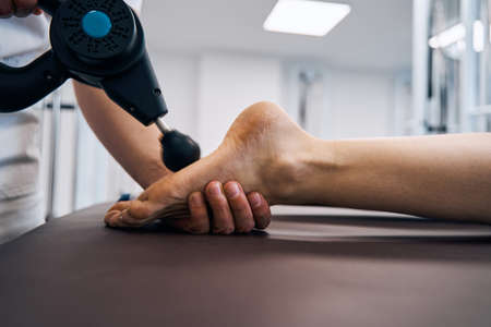 Close-up of masseur rubbing woman foot with massage percussion device in rehab clinics therapy roomの写真素材