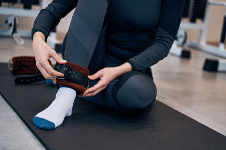 Pretty caucasian woman in black sportwear wearing cuffs of ankle support. Protection and anti-sprain