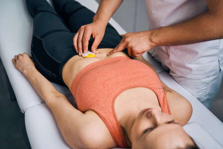 Therapist placing electrostimulator on woman stomach. Specialist in massage parlor puts electrodesの写真素材