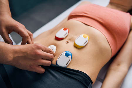 Close-up of electric stimulator on woman stomach. Physiotherapy electrodes for myostimulationの写真素材
