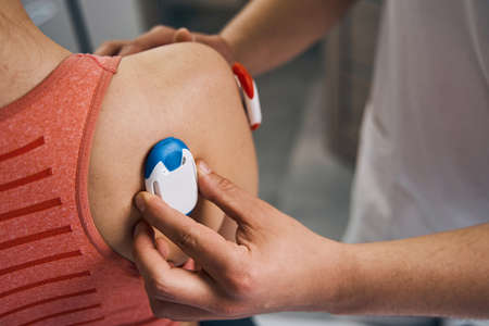 Close-up massage therapist placing electrostimulator on woman shoulder. Physiotherapy myostimulation