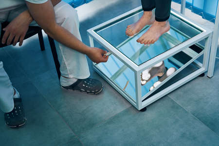 Girl bare feet close-up inspection for flatfoot with plantoscopy with therapist in office. Womanの写真素材