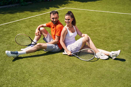 Athletic couple with rackets seated on the tennis courtの写真素材
