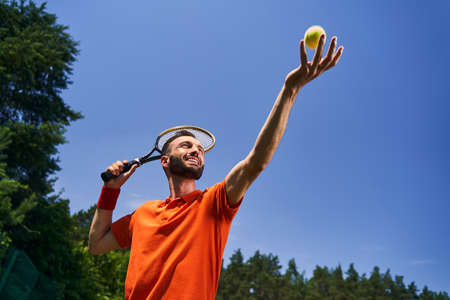 Male tennis player tossing the ball into the airの写真素材