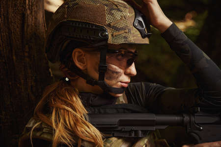 Beautiful woman in helmet using weapon in forest