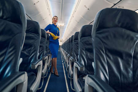 Happy attractive flight attendant standing in the cabin aisle