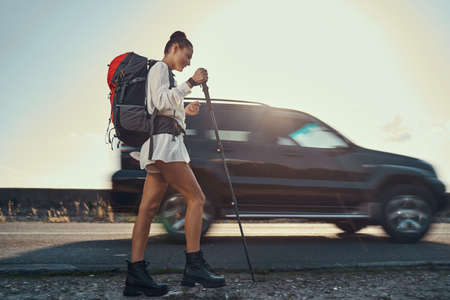 Joyful traveller hiking with walking poles on roadside