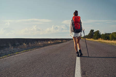 Back view of tourist moving on asphalt roadの写真素材