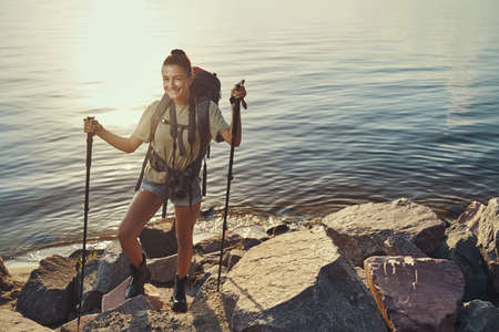 Happy hiker smiling at camera while standing on lakeside rocks