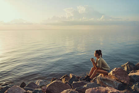 Person having a drink at the lake shore at sunsetの写真素材