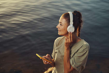 Female pressing headphones closer while enjoying music in natureの写真素材